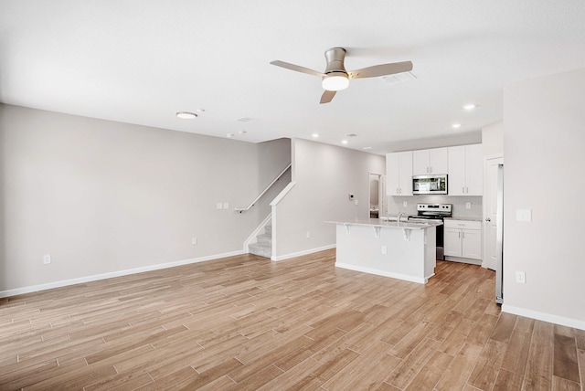 kitchen featuring a breakfast bar area, appliances with stainless steel finishes, light hardwood / wood-style floors, an island with sink, and white cabinets