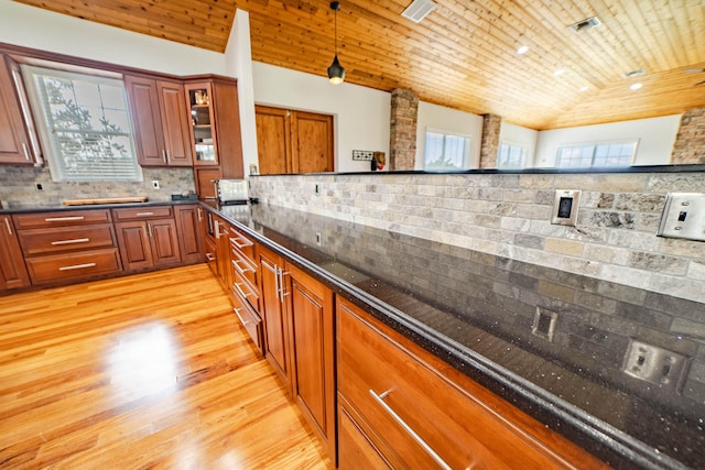 kitchen with decorative backsplash, light hardwood / wood-style flooring, dark stone countertops, hanging light fixtures, and lofted ceiling