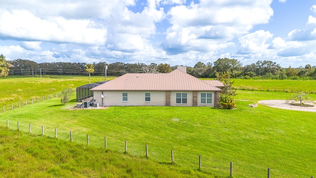 rear view of house featuring a lanai, a rural view, and a lawn