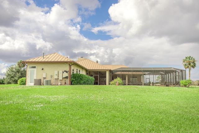 rear view of house with a lawn, glass enclosure, and central AC