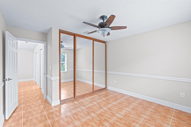 unfurnished bedroom with ceiling fan, light tile patterned flooring, a textured ceiling, and a closet