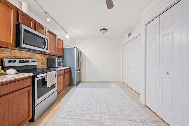 kitchen with light tile patterned flooring, track lighting, light stone counters, appliances with stainless steel finishes, and decorative backsplash