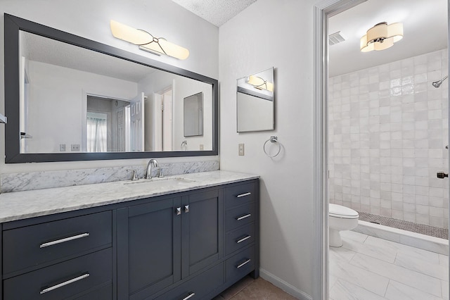 bathroom featuring a tile shower, vanity, a textured ceiling, and toilet