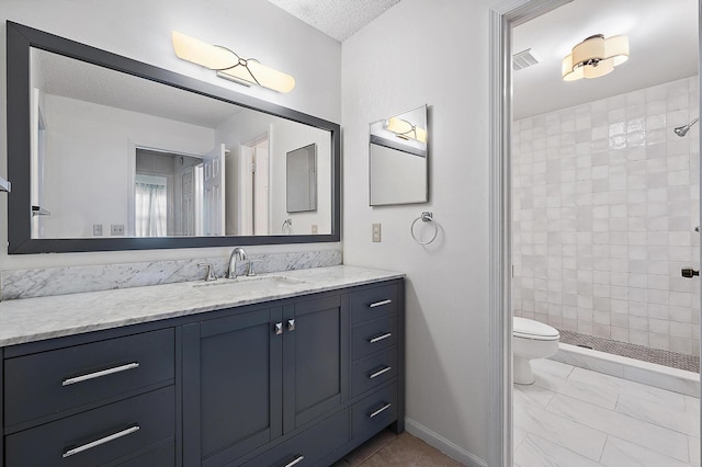 bathroom featuring tiled shower, vanity, toilet, baseboards, and a textured ceiling