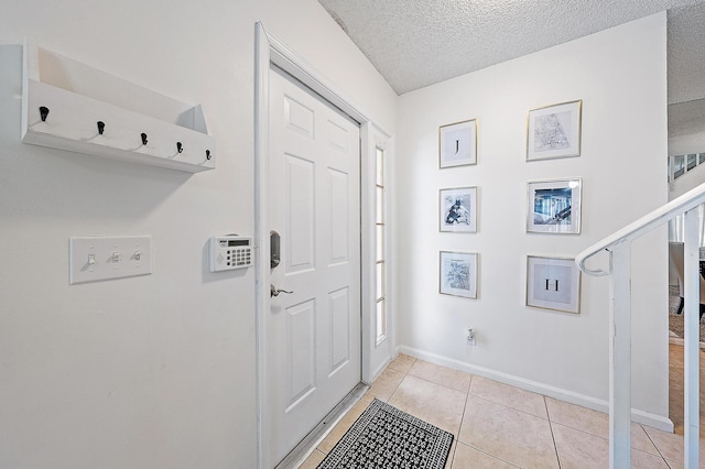 entryway featuring light tile patterned floors, a textured ceiling, and baseboards