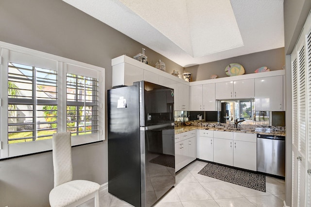 kitchen featuring black fridge, dishwasher, sink, light tile patterned flooring, and white cabinetry