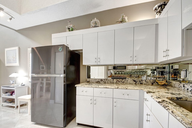 kitchen with light stone countertops, black refrigerator, a textured ceiling, and white cabinetry