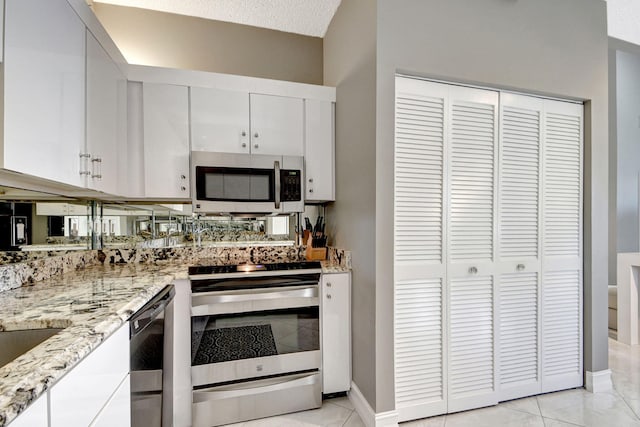 kitchen featuring stainless steel appliances, light stone counters, a textured ceiling, light tile patterned floors, and white cabinets