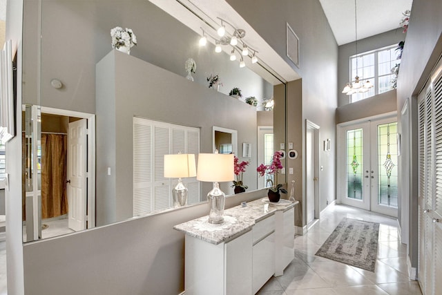 bathroom featuring a towering ceiling, tile patterned floors, an inviting chandelier, and french doors