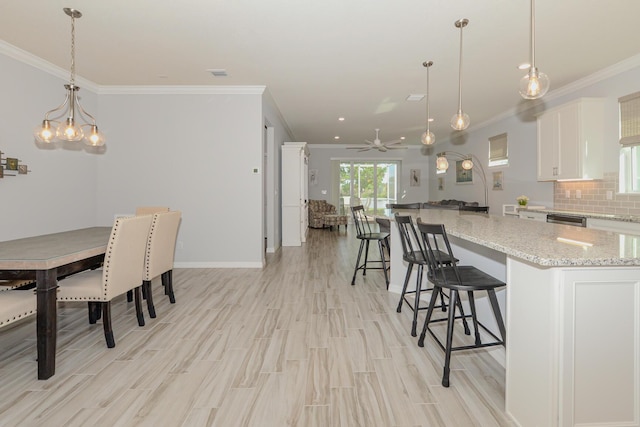 kitchen with light stone counters, ceiling fan with notable chandelier, decorative light fixtures, white cabinets, and a center island