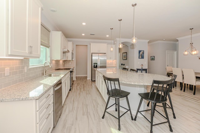 kitchen with white cabinetry, a center island, hanging light fixtures, stainless steel appliances, and backsplash