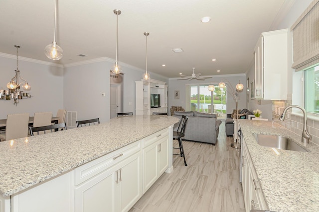 kitchen featuring a center island, ceiling fan with notable chandelier, sink, white cabinetry, and a breakfast bar area