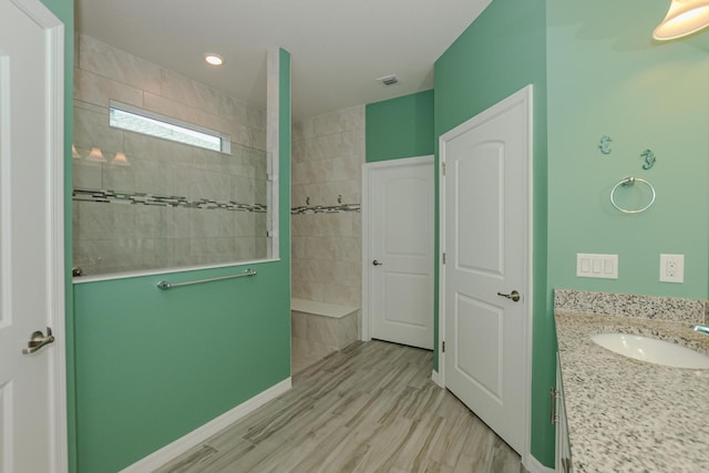 bathroom featuring a tile shower, vanity, and wood-type flooring