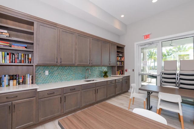 kitchen with light wood-type flooring, tasteful backsplash, dark brown cabinetry, and sink