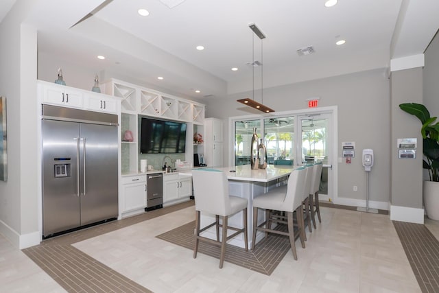 kitchen with a center island with sink, a kitchen breakfast bar, stainless steel built in fridge, decorative light fixtures, and white cabinetry