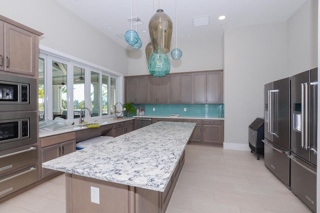 kitchen with decorative backsplash, light stone countertops, a towering ceiling, stainless steel appliances, and a center island