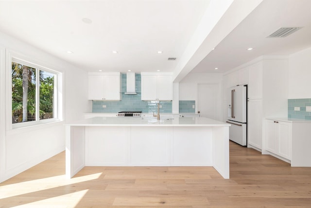 kitchen featuring high end white refrigerator, wall chimney range hood, white cabinets, and light hardwood / wood-style floors