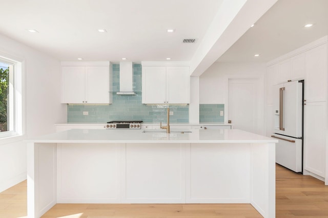 kitchen with a kitchen island with sink, white cabinets, high end white refrigerator, and wall chimney exhaust hood