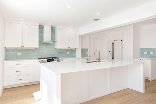 kitchen featuring sink, high end white refrigerator, wall chimney range hood, and a center island with sink