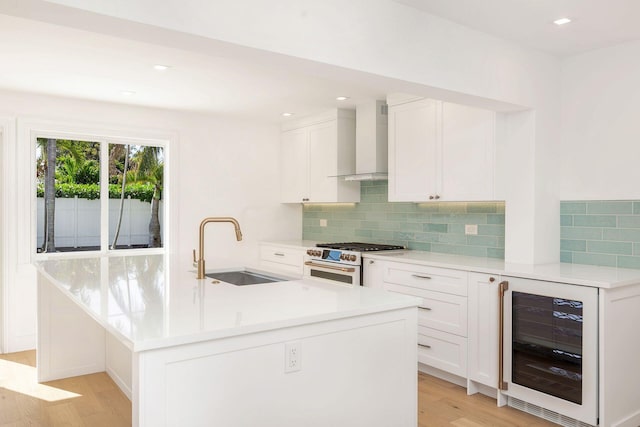 kitchen featuring sink, high end white range, white cabinets, beverage cooler, and wall chimney exhaust hood