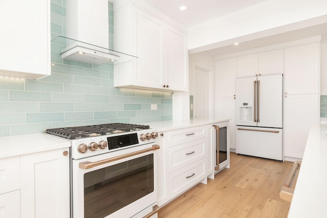 kitchen with wall chimney exhaust hood, white cabinetry, tasteful backsplash, light hardwood / wood-style flooring, and white appliances