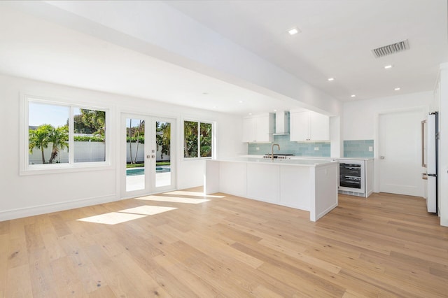 kitchen featuring wall chimney range hood, sink, white cabinetry, wine cooler, and decorative backsplash