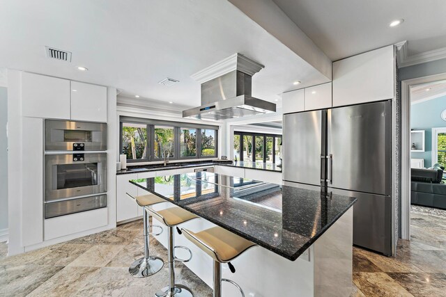 kitchen featuring a kitchen bar, appliances with stainless steel finishes, white cabinetry, and island range hood