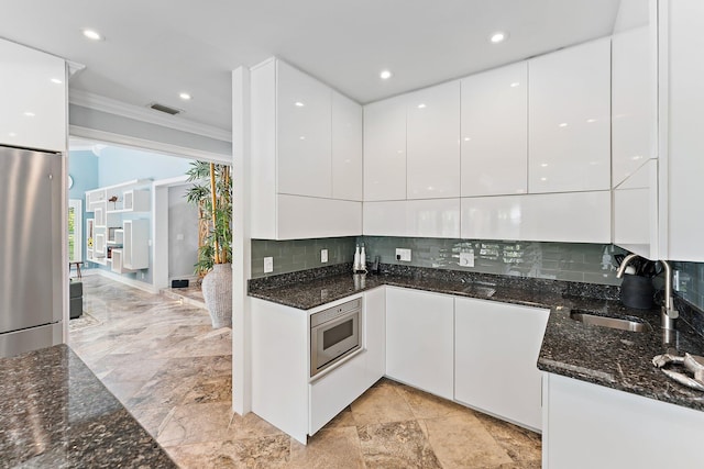 kitchen with white cabinetry, dark stone countertops, decorative backsplash, ornamental molding, and stainless steel appliances