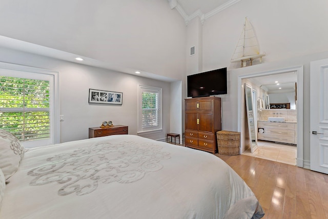 bedroom with ornamental molding, light wood-type flooring, and a towering ceiling