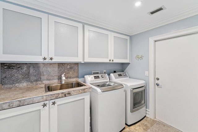 clothes washing area with sink, crown molding, washer and clothes dryer, and cabinets