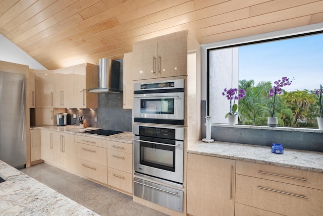 kitchen featuring light brown cabinetry, wall chimney range hood, lofted ceiling, and light stone countertops