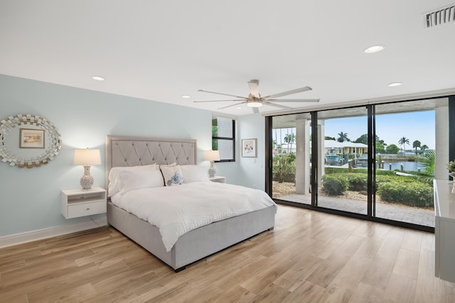 bedroom featuring expansive windows, a water view, access to exterior, ceiling fan, and light wood-type flooring