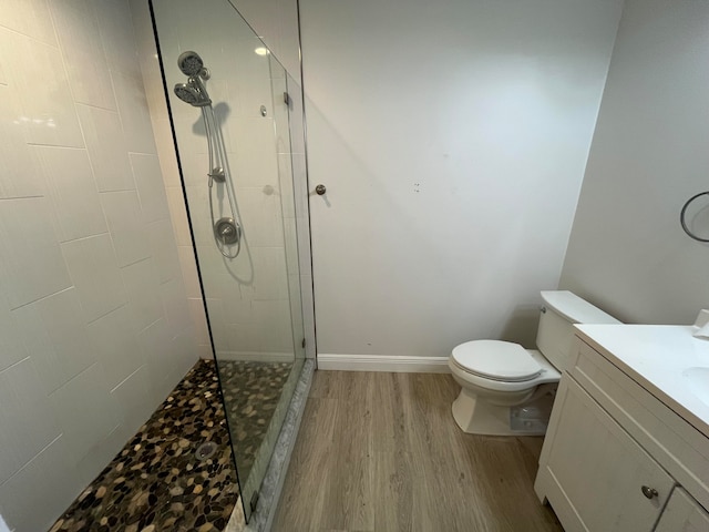 bathroom with hardwood / wood-style flooring, vanity, toilet, and tiled shower