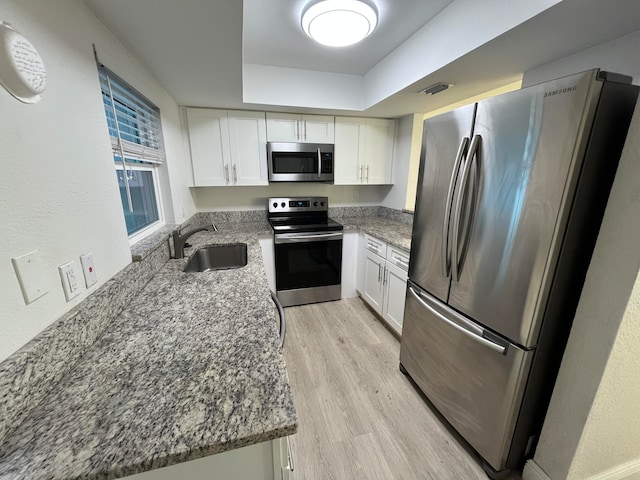 kitchen with stone counters, sink, light wood-type flooring, appliances with stainless steel finishes, and white cabinetry