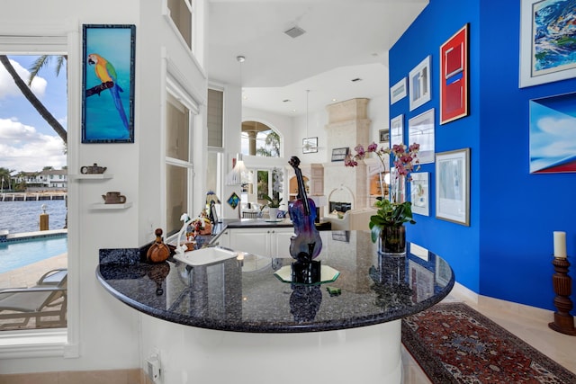 bar featuring white cabinets, decorative light fixtures, dark stone countertops, and sink