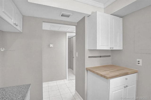 kitchen with wooden counters, white cabinetry, light tile patterned floors, and crown molding