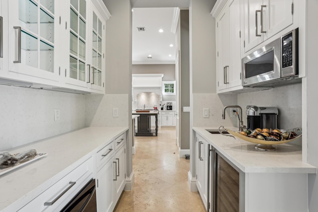 kitchen with backsplash, light stone counters, ornamental molding, sink, and white cabinetry