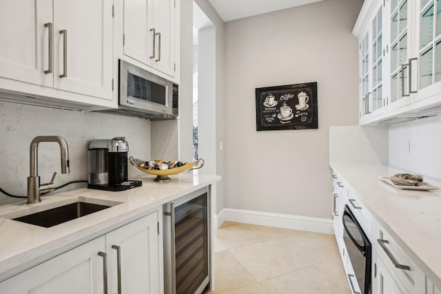 kitchen featuring light stone countertops, beverage cooler, sink, light tile patterned floors, and white cabinets