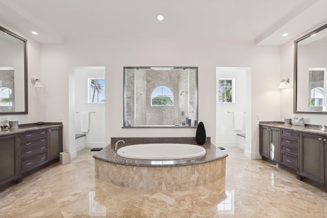 bathroom with a wealth of natural light, vanity, and a relaxing tiled tub