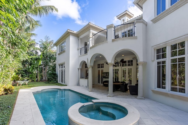 rear view of property with outdoor lounge area, french doors, a pool with hot tub, a balcony, and a patio area