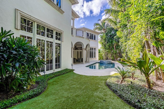 back of house featuring a lawn, a patio area, a balcony, and a pool with hot tub