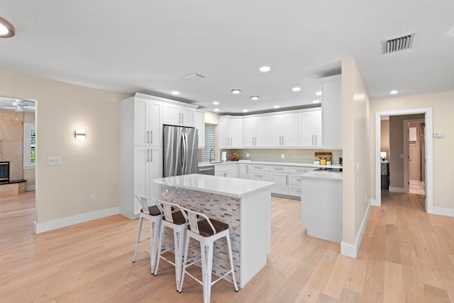 kitchen featuring a tile fireplace, white cabinetry, a kitchen bar, appliances with stainless steel finishes, and light wood-type flooring