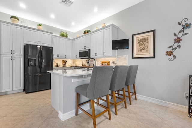 kitchen featuring kitchen peninsula, tasteful backsplash, black fridge, a breakfast bar, and white cabinets