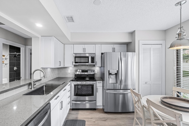 kitchen featuring sink, light stone counters, white cabinets, stainless steel appliances, and backsplash