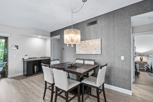 dining area featuring an inviting chandelier, a textured ceiling, and light wood-type flooring