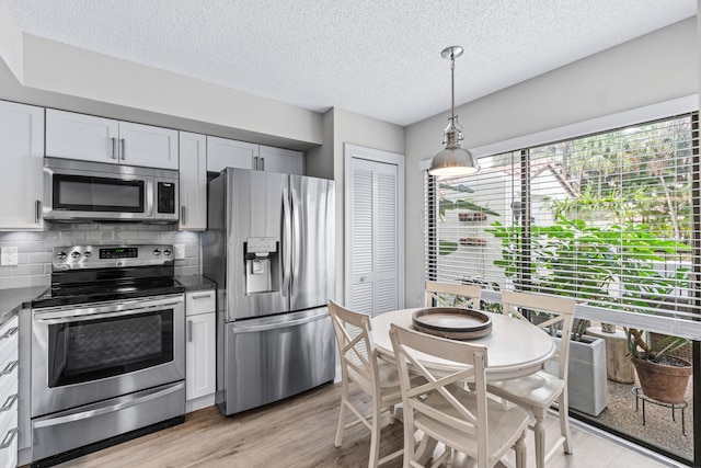 kitchen with decorative light fixtures, decorative backsplash, stainless steel appliances, and white cabinets