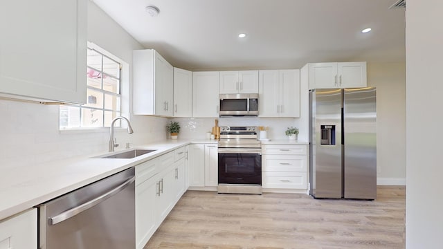 kitchen with stainless steel appliances, white cabinetry, sink, and light hardwood / wood-style flooring