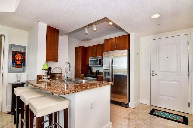 kitchen with kitchen peninsula, stainless steel appliances, a textured ceiling, and dark stone countertops