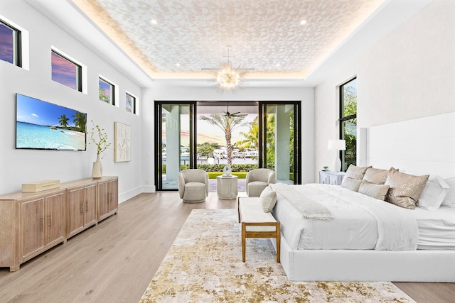 bedroom with access to outside, ceiling fan with notable chandelier, light wood-type flooring, and a tray ceiling