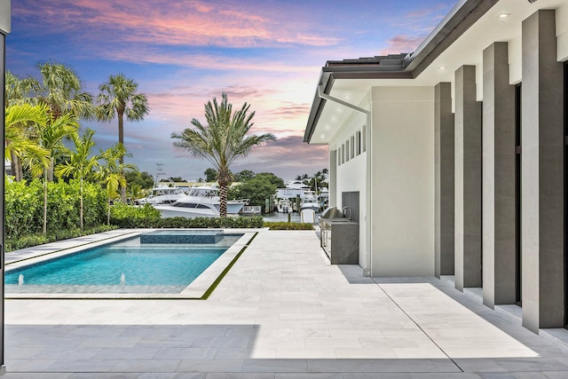 pool at dusk featuring a patio, an outdoor kitchen, and an in ground hot tub